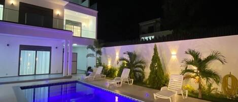 Une maison moderne à deux étages, dotée d’une piscine, d’un espace extérieur aménagé et d’un éclairage extérieur soigné.