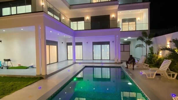 A modern two-story house with a swimming pool, outdoor seating, and a well-lit balcony. - Teranga Blue (Ngaparou)