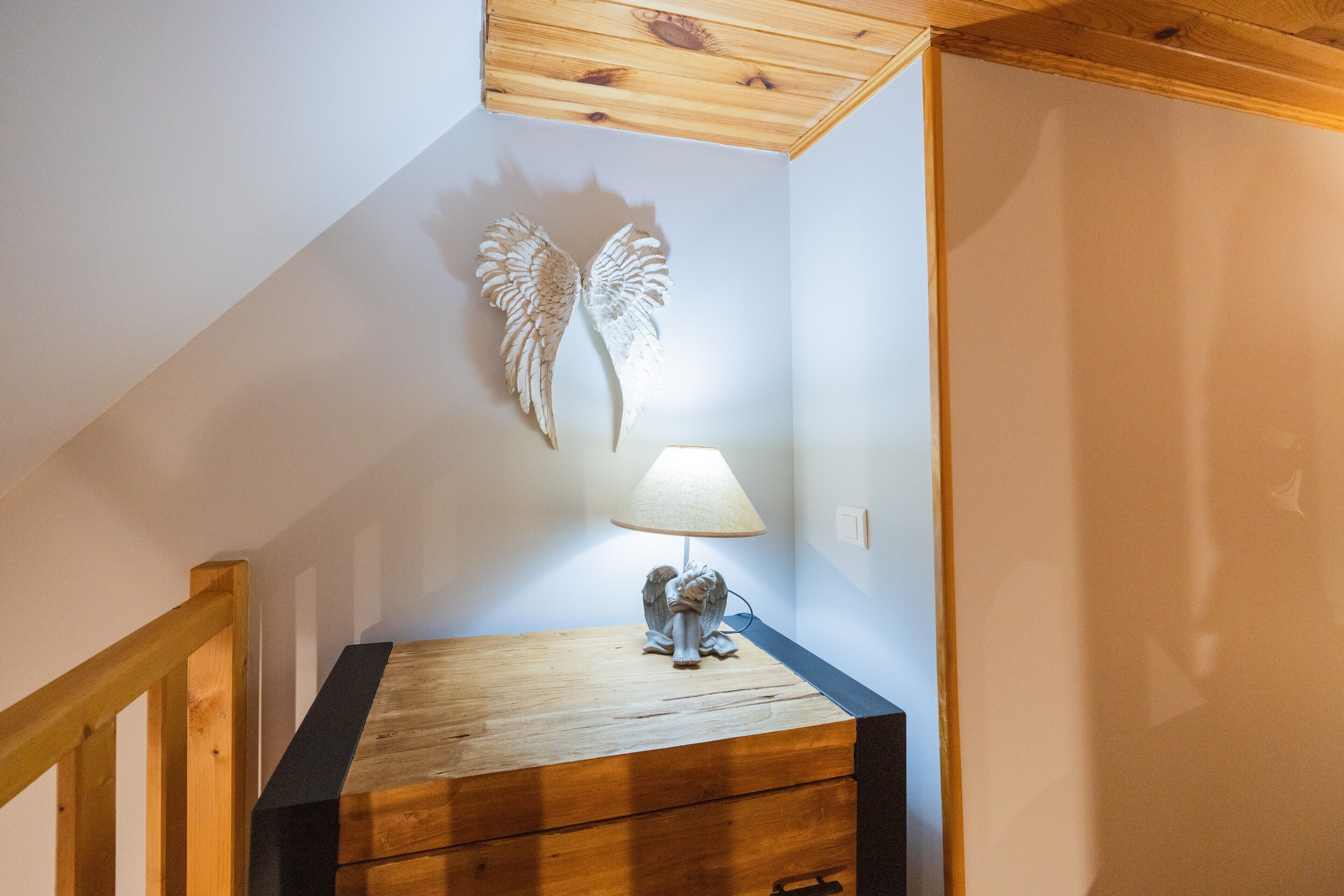 Een trap met houten leuning, een wandlamp en een decoratief engelbeeldje op een houten kist.