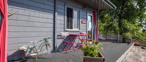 Um deck de madeira com uma bicicleta, uma cadeira vermelha e um vaso com plantas verdes.