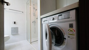 Un baño moderno con ducha de vidrio, un inodoro blanco y una lavadora de carga frontal.