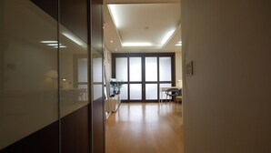 Un pasillo con suelo de madera, una partición de vidrio y una puerta que da a una habitación con un ventanal grande.