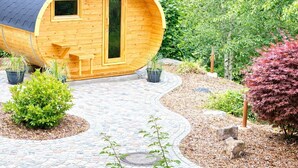 A wooden cabin with a curved roof, a door, and windows, surrounded by a landscaped garden with potted plants and a stone pathway. - Holiday Home Feldberg in the Black Forest with Mountain Views, Terrace and Wi-Fi (Feldberg-Falkau)