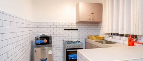 A compact kitchen with white tiled walls, a built-in oven, a gas stove, and a refrigerator.