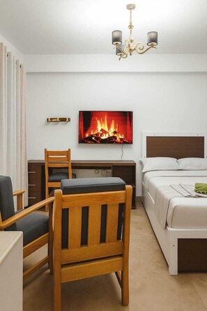 A hotel room with a bed, a desk with a chair, a television displaying a fireplace, and a chandelier. - Nanyuki Cozy Haven Studio Apartments (Nanyuki)