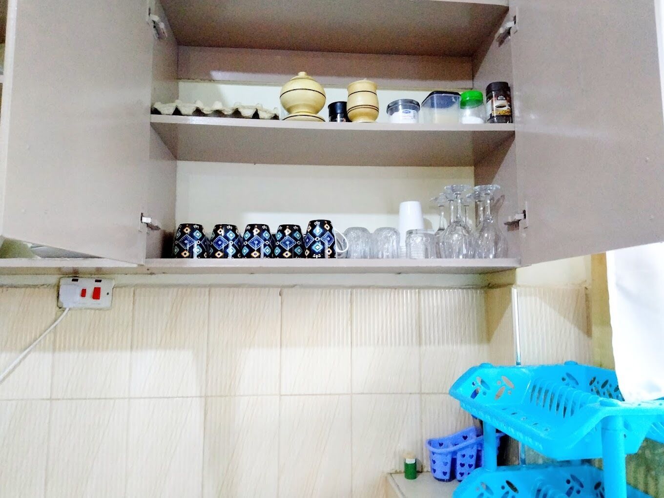 A kitchen with a cabinet containing kitchenware and utensils.