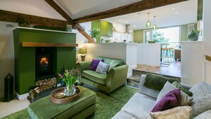 Ein gemütliches Wohnzimmer mit Kamin, grünen Sofas und einem Essbereich im Hintergrund.