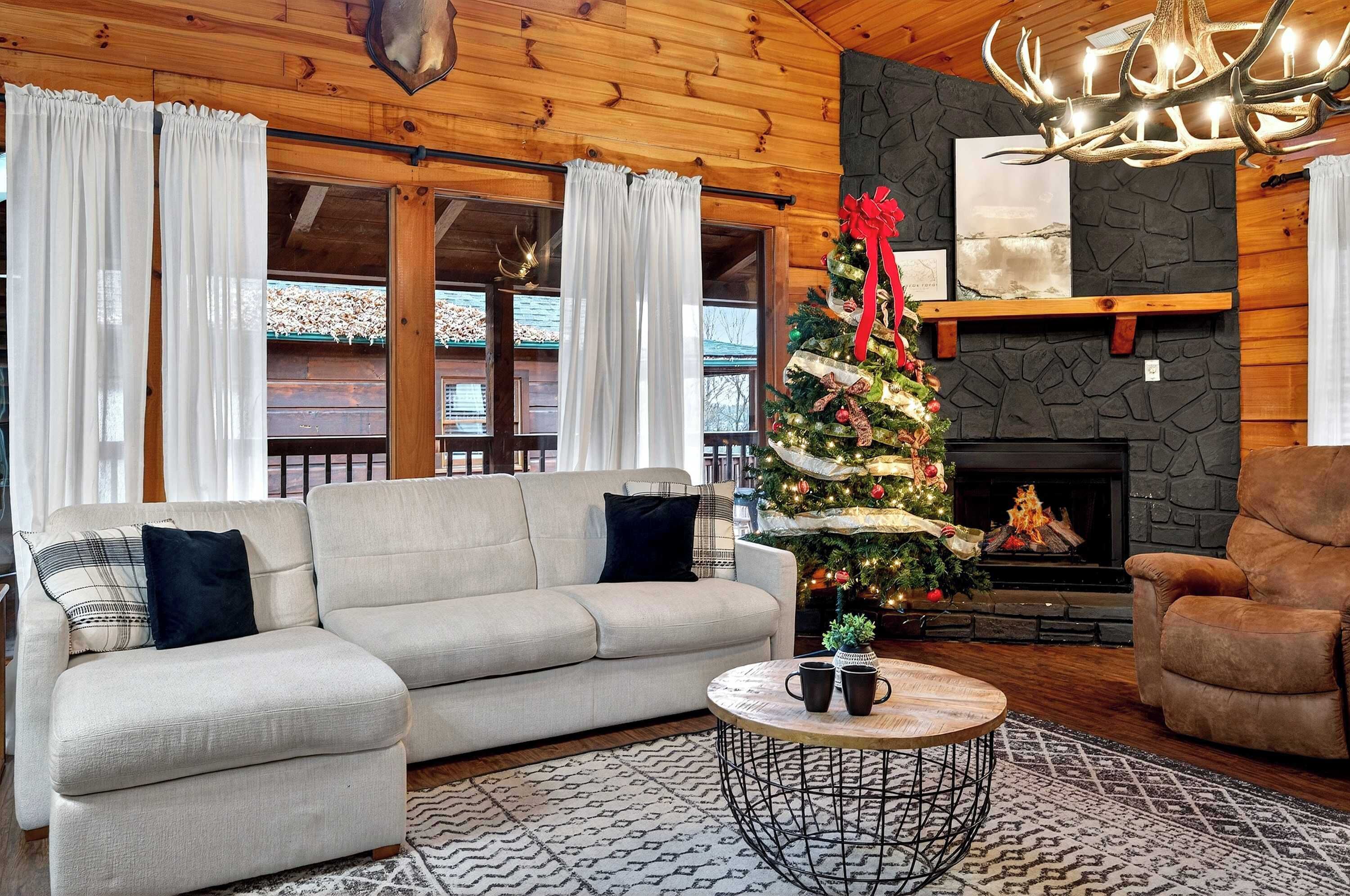 Ein gemütliches Wohnzimmer mit einer Couch, einem Sessel und einem Kamin. Ein Weihnachtsbaum ist mit Dekorationen und Lichterketten geschmückt.