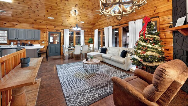 L’intérieur d’un chalet accueillant, avec un plafond en bois, un coin repas, un salon décoré d’un sapin de Noël et une cheminée.