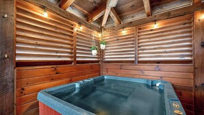 Une cabane en bois dotée d’un bain à remous, de murs en bois et de luminaires suspendus.