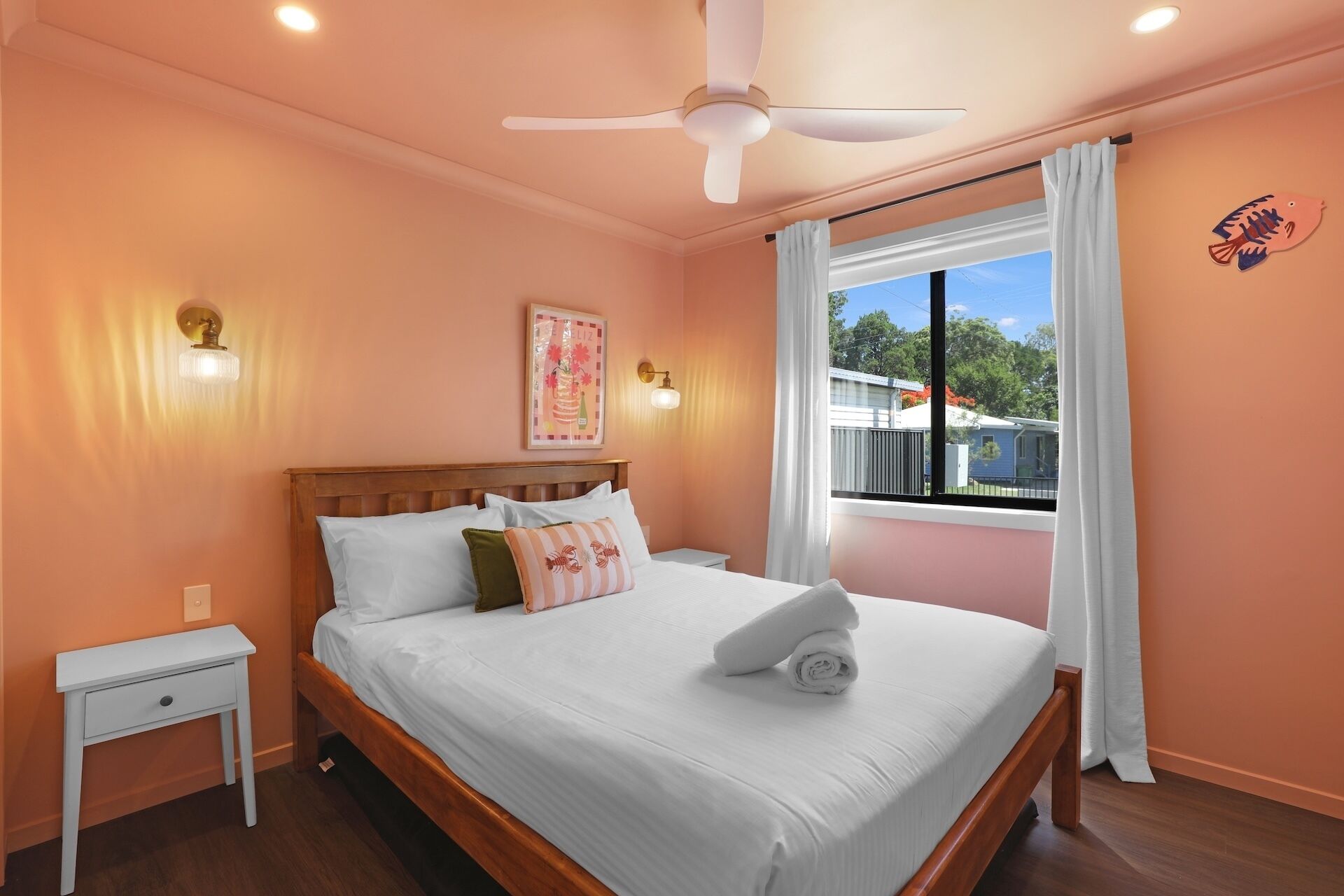 Une chambre à coucher avec un lit, une table de chevet, un ventilateur de plafond et une fenêtre avec des rideaux.