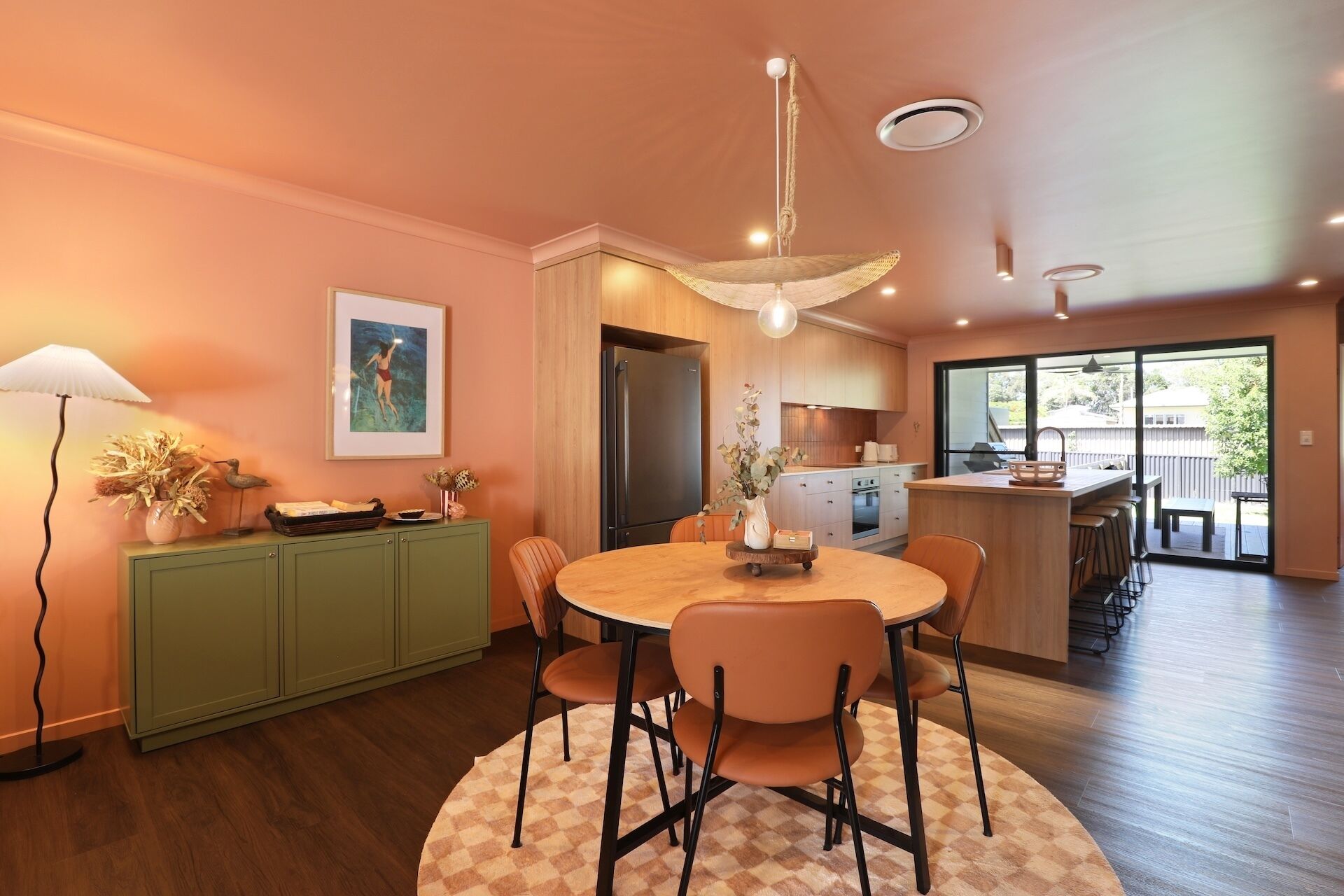 A modern kitchen with a central island, wooden cabinets, and a dining area with a round table and chairs.