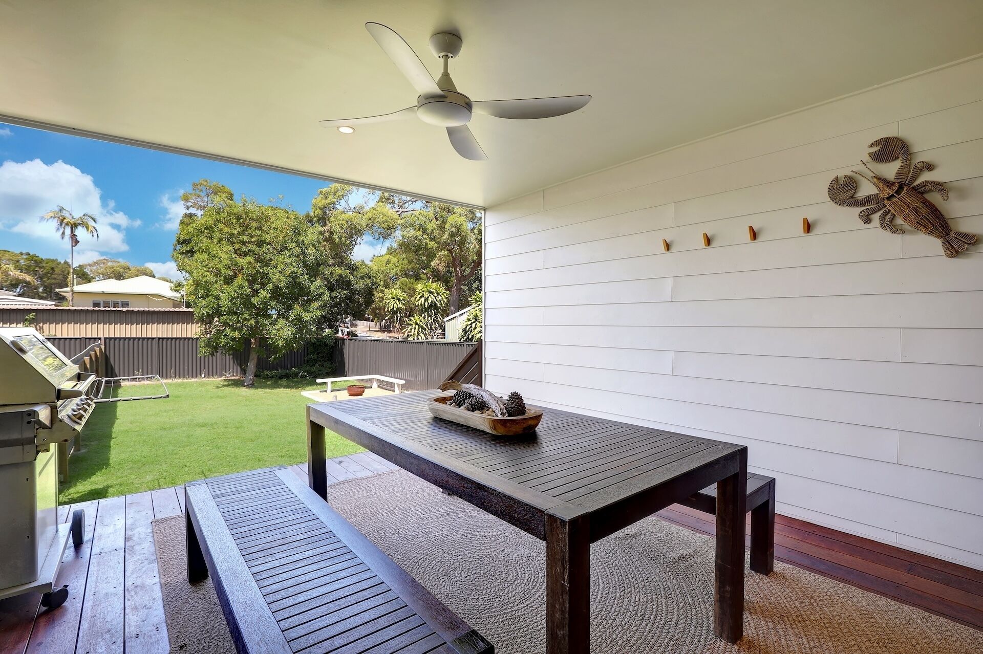 Eine Terrasse mit Holztisch und Bank, einem Deckenventilator und einem dekorativen Wandelement.