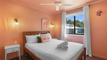 Ein Schlafzimmer mit einem Bett, einem Nachttisch, einem Deckenventilator und einem Fenster mit Vorhängen.