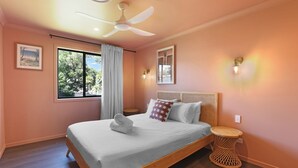 Ein Schlafzimmer mit Bett, Deckenventilator, Fenster mit Vorhängen und einer Wandleuchte.
