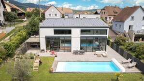 A modern house with a swimming pool, a patio with outdoor furniture, and a view of neighboring houses.