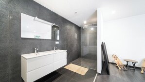 A modern bathroom with a large mirror, two sinks, a shower, and a small table with chairs.