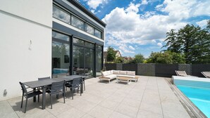 A modern outdoor patio with a pool, a dining area, and a seating arrangement.
