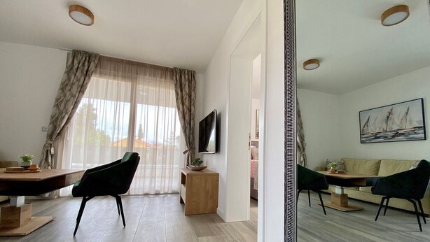 A modern living room with a large mirror, a TV, a sofa, and a dining area with chairs and a table. - Premium 4 stars Apartment Krk, 5 min to Beach & City Center, Smart TV, Netflix (Krk)