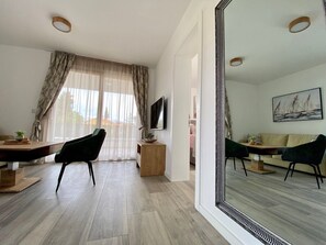 A modern living room with a large mirror, a TV, a sofa, and a dining area with chairs and a table. - Premium 4 stars Apartment Krk, 5 min to Beach & City Center, Smart TV, Netflix (Krk)