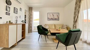 A modern living room with a sofa, two green chairs, a wooden coffee table, and a dining area with a wooden cabinet and a clock. - Premium 4 stars Apartment Krk, 5 min to Beach & City Center, Smart TV, Netflix (Krk)