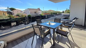A modern outdoor patio with a table and chairs, a glass balustrade, and a view of surrounding buildings and greenery. - Premium 4 stars Apartment Krk, 5 min to Beach & City Center, Smart TV, Netflix (Krk)