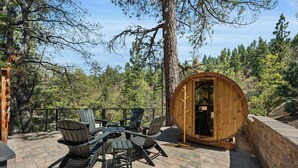 Une structure en forme de tonneau en bois, des sièges d’extérieur avec des fauteuils Adirondack et un patio entouré d’arbres.