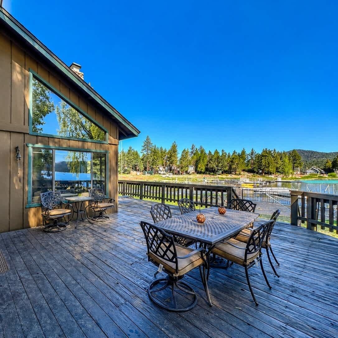 A wooden deck with a table and chairs, overlooking a body of water and a forested area.