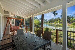 Ein überdachter Patio mit Tisch und Stühlen, mit Blick auf einen See und einen Wald.