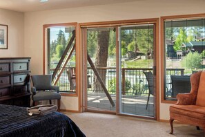 Ein Zimmer mit einem Bett, einem Sessel, einem Sofa, einer Kommode und großen Schiebeglastüren, die zu einem Außenbereich mit Terrasse und einer Treppe führen.