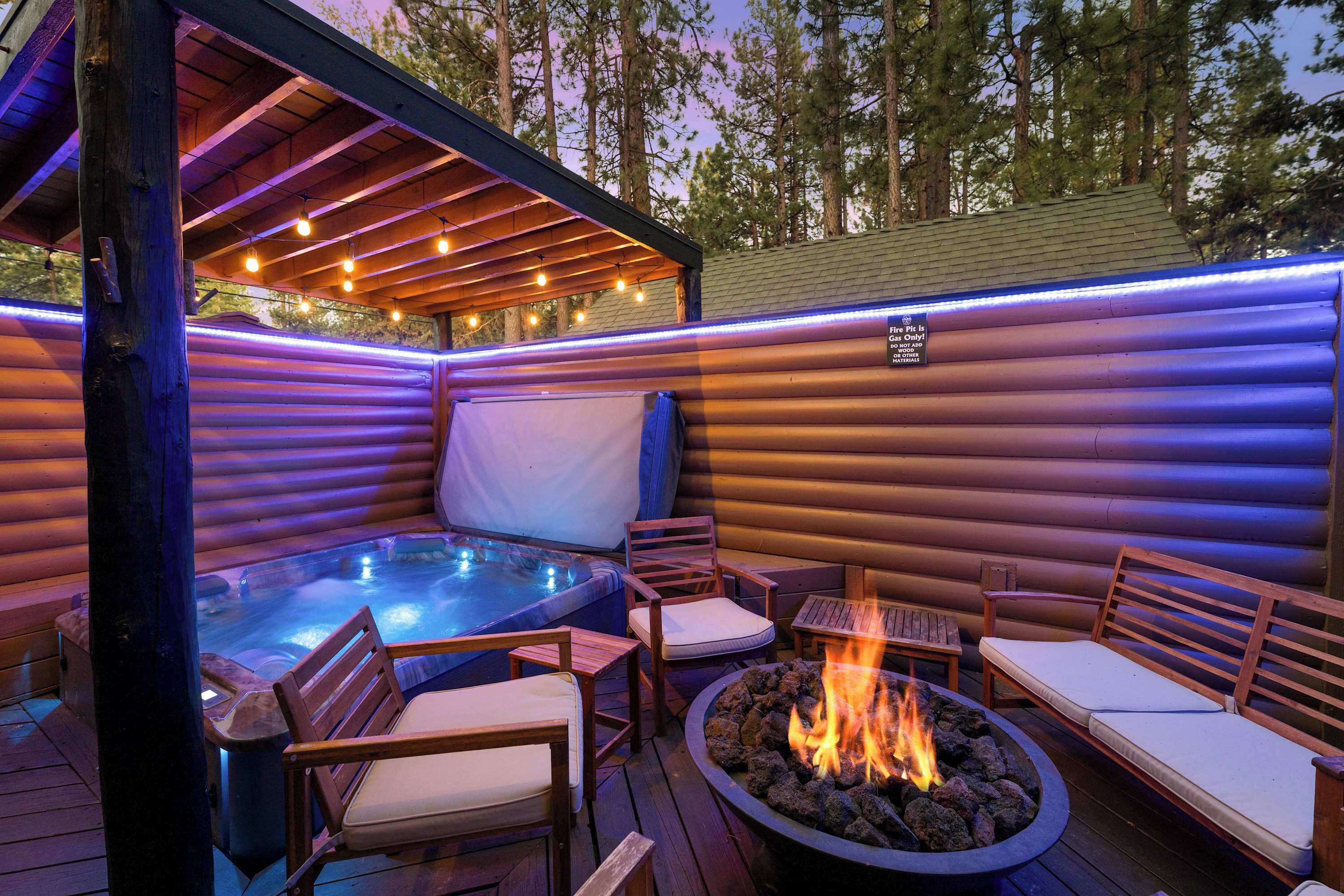 A log cabin with a hot tub, outdoor seating, and a fire pit.