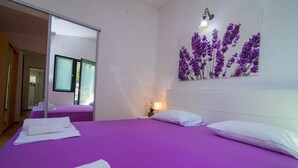 Quarto de hotel com uma cama grande, duas camas menores, um espelho, luminária na parede e uma obra de arte floral.
