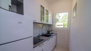 Uma cozinha compacta com geladeira branca, pia com torneira moderna e janela que permite entrada de luz natural.