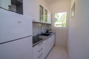 Eine kleine Küche mit einem weißen Kühlschrank, einem Waschbecken mit modernem Wasserhahn und einem Fenster, das für natürliches Licht sorgt.