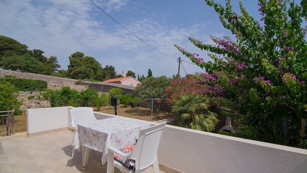 En udendørs terrasse med et bord og stole, omgivet af grøn vegetation og en stenvæg.
