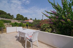 En udendørs terrasse med et bord og stole, omgivet af grøn vegetation og en stenvæg.