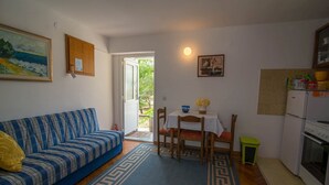 En kompakt opholdsstue med sofa, spisebord, stole og et tekøkken.