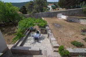Un patio de piedra con una mesa y sillas, rodeado de plantas en macetas y un enrejado.