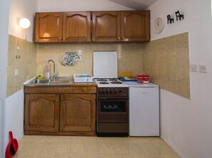 Eine kompakte Küche mit Holzschränken, einem Gaskochfeld, einem Backofen und einem kleinen Kühlschrank.