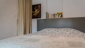 A bedroom with a bed, a painting, a bookshelf, and a window with curtains.