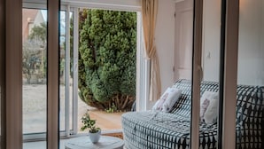 Un salon moderne avec un canapé, une petite table ronde et une vue sur un jardin, visible à travers une porte vitrée.