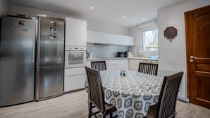 Une cuisine moderne équipée d’appareils électroménagers en acier inoxydable, une table à manger recouverte d’une nappe à motifs et des chaises en bois.