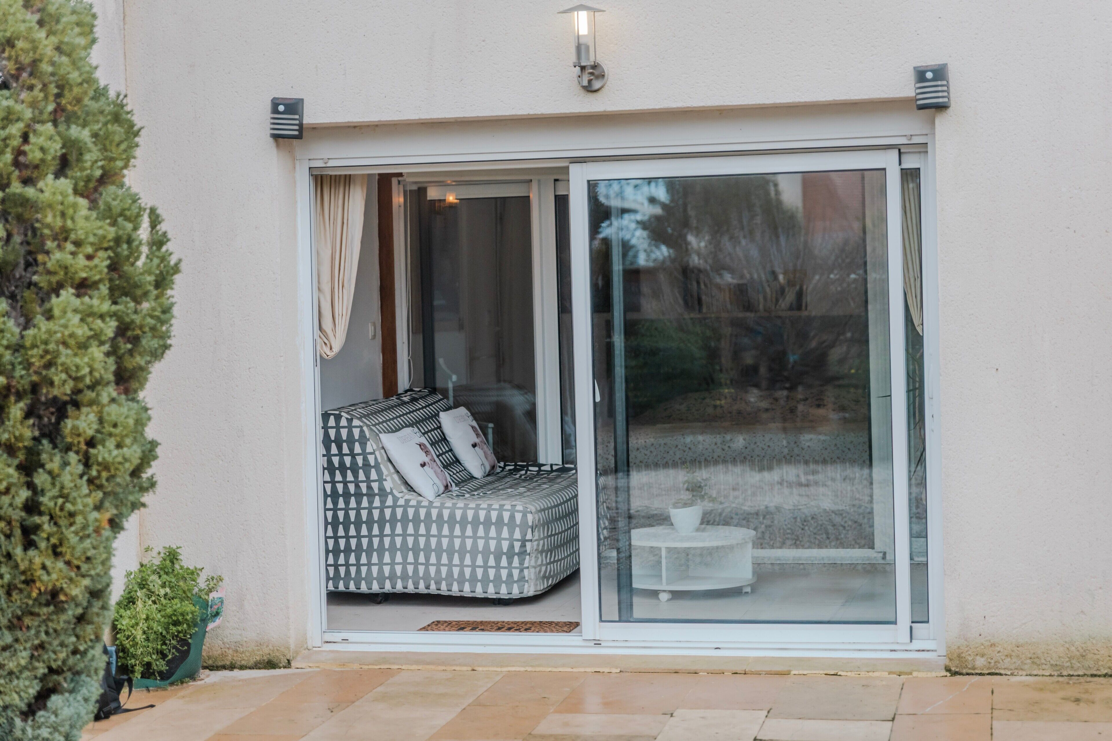 A modern house with a sliding glass door leading to a patio area with a patterned sofa and a small table.