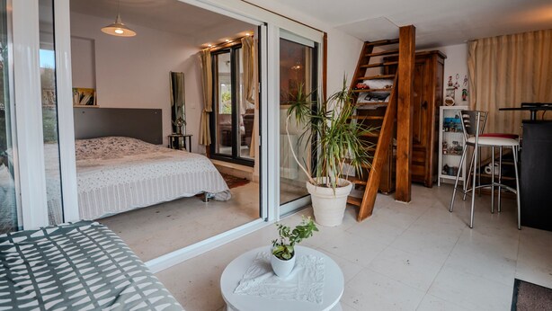 Une chambre moderne avec un lit, une table ronde agrémentée d’une plante, une chaise, une échelle et un bureau avec une chaise.