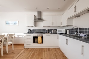 A modern kitchen with white cabinetry, a built-in oven, a microwave, and a gas stove. - Kingsmuir | Elie | 4 Bedroom House (Elie)