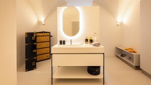 Un baño moderno con un tocador blanco, un espejo grande y un baúl negro y dorado.