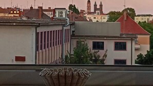 A cityscape with a prominent tower in the background, a building with a red roof, and a decorative bowl on a ledge. - Apartment with Cathedral View in Hradec Králové (Hradec Králové)