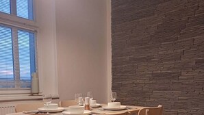 A dining area with a wooden table and chairs, a stone-textured wall, and a window with blinds. - Apartment with Cathedral View in Hradec Králové (Hradec Králové)