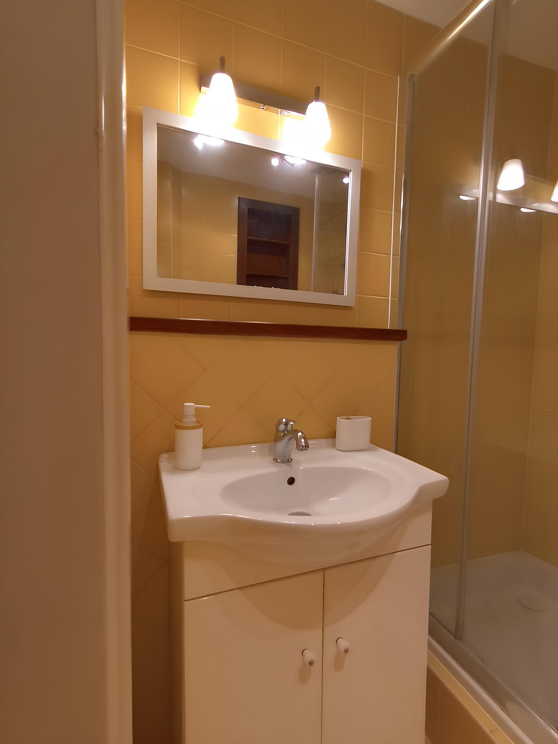 A bathroom with a white sink, a mirror with lights, and a glass shower enclosure.
