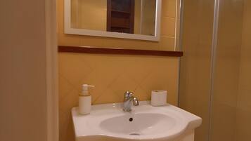 A bathroom with a white sink, a mirror with lights, and a glass shower enclosure.